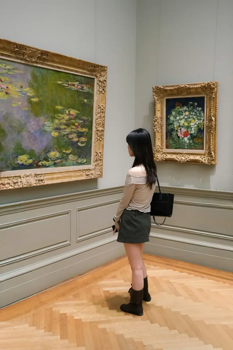 Bir sanat galerisinde duvarda asılı tabloları inceleyen bir kadın ziyaretçi