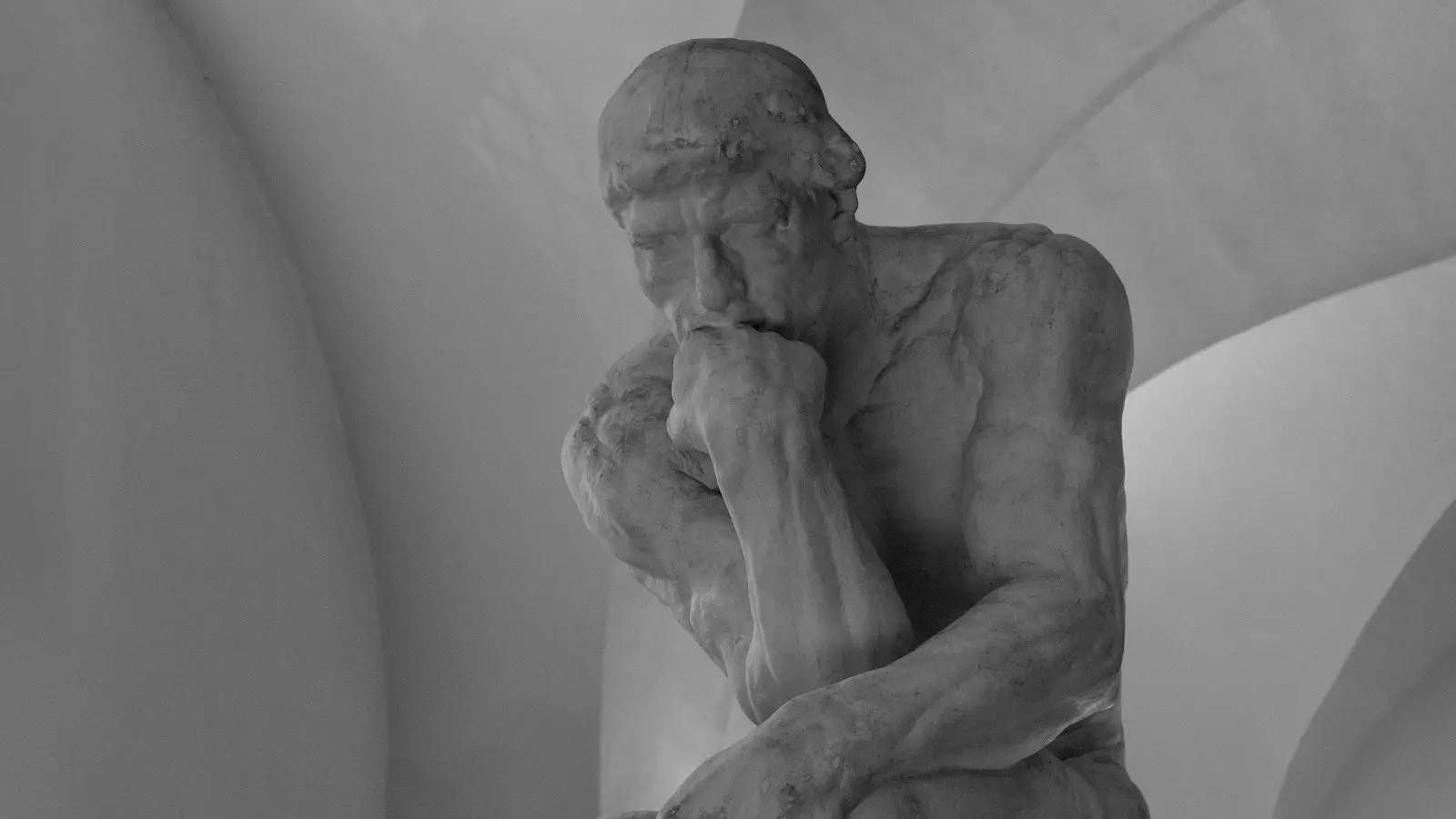 Auguste Rodin’in Düşünen Adam heykelinin siyah beyaz fotoğrafı: çenesini eline dayamış, oturan figür