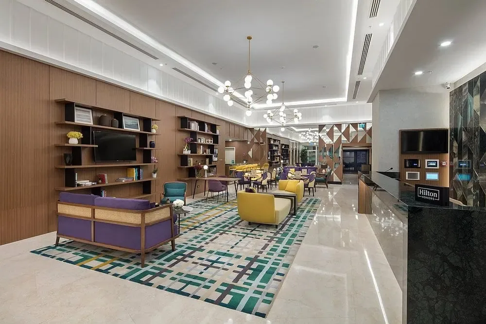 DoubleTree by Hilton Afyonkarahisar lobisi: halılı oturma alanı, geniş kitaplık duvarı ve sağda resepsiyon